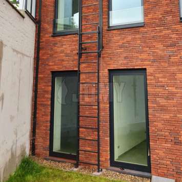 Fire escape vertical sliding ladder without safety cage and wall-mounted on a brick wall.